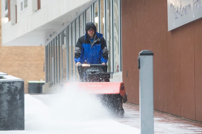 A man sweeps away snow on the sidewalk in front of The Residences at Mid-town Park in downtown Wilmington Thursday, Feb. 18, 2021.
