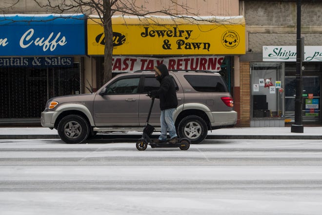 A woman rides an electric scooter up Market Street in the snow Thursday, Feb. 18, 2021.